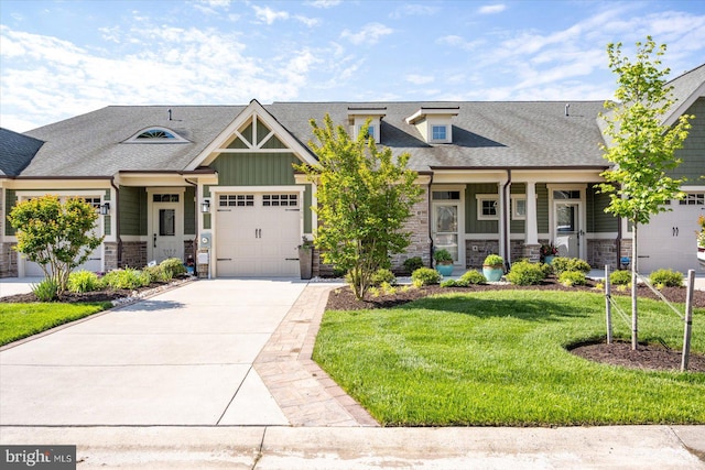 craftsman house featuring stone siding, concrete driveway, a front yard, an attached garage, and roof with shingles