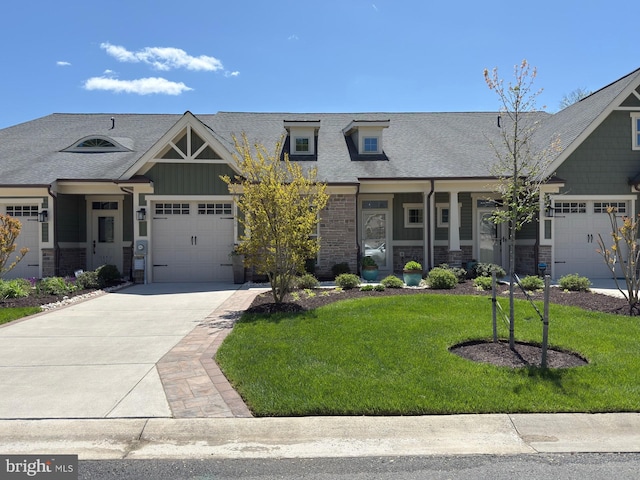 craftsman-style home featuring a front yard, driveway, roof with shingles, an attached garage, and stone siding