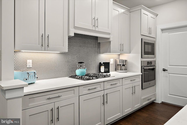kitchen featuring stainless steel appliances, decorative backsplash, light countertops, and dark wood finished floors