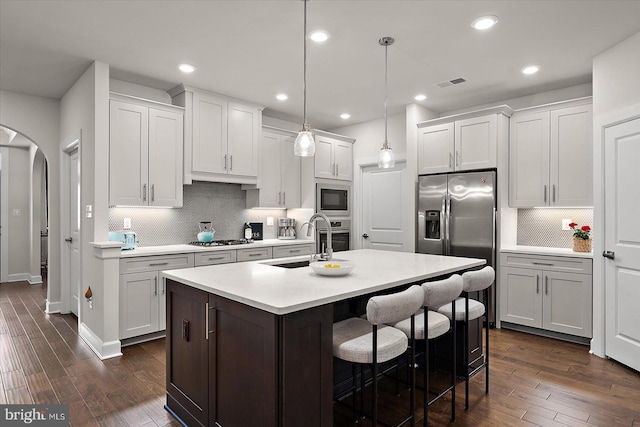 kitchen with arched walkways, stainless steel appliances, a sink, light countertops, and dark wood finished floors