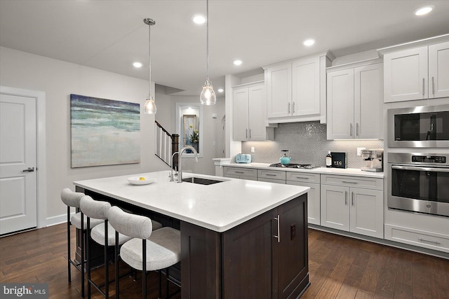 kitchen with appliances with stainless steel finishes, a sink, light countertops, dark wood-style floors, and a center island with sink