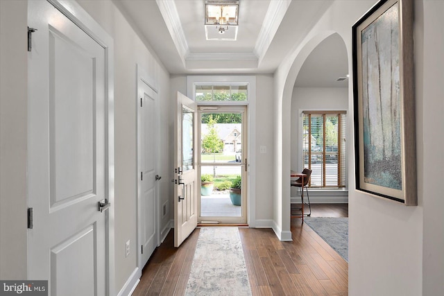 entrance foyer with dark wood-style flooring, a tray ceiling, crown molding, arched walkways, and baseboards