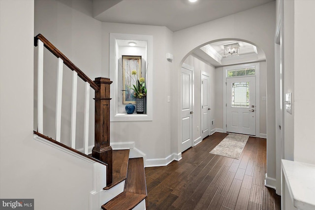 foyer entrance featuring dark wood finished floors, stairs, baseboards, arched walkways, and ornamental molding