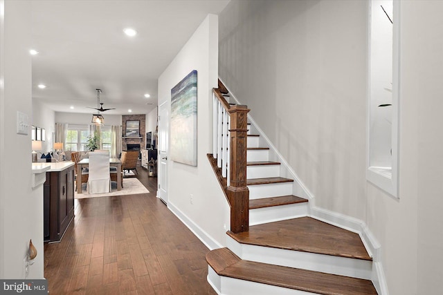 stairs with wood finished floors, recessed lighting, a ceiling fan, baseboards, and a fireplace