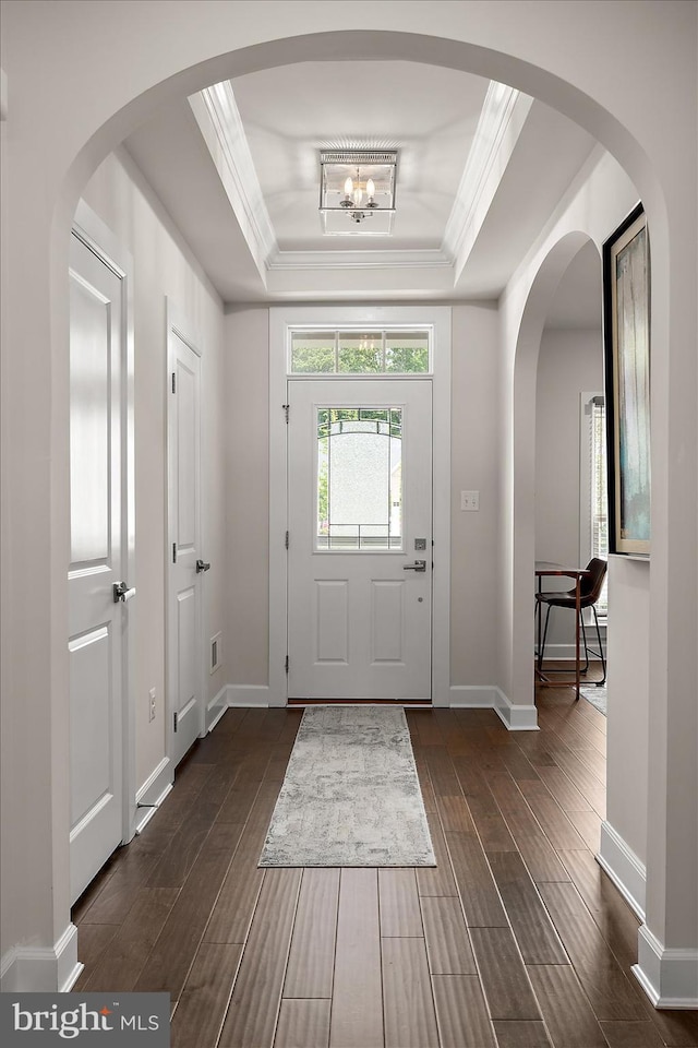 entryway with dark wood finished floors, a raised ceiling, crown molding, baseboards, and a chandelier