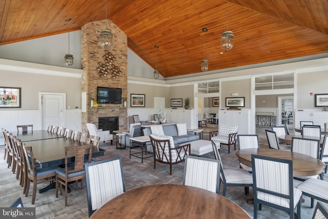 dining room with high vaulted ceiling, wood ceiling, a wainscoted wall, a large fireplace, and a decorative wall