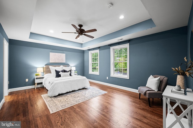 bedroom featuring a tray ceiling, baseboards, wood finished floors, recessed lighting, and a ceiling fan