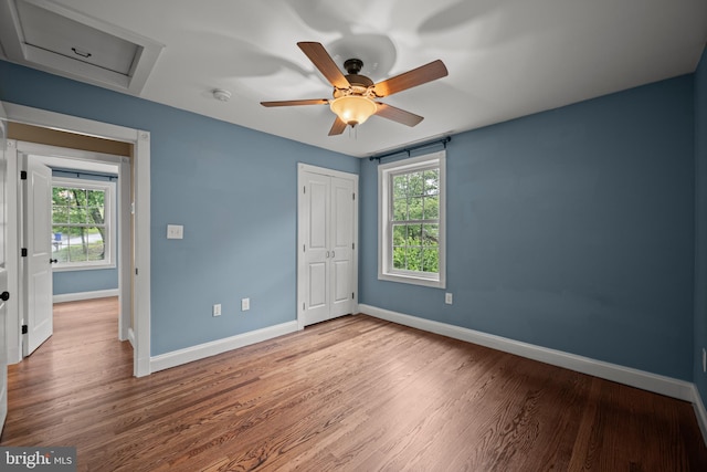unfurnished bedroom with baseboards, wood finished floors, a closet, and attic access