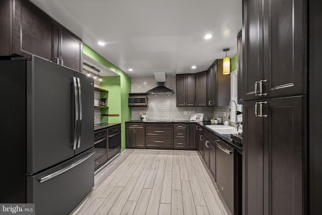 kitchen with stainless steel appliances, a sink, wall chimney exhaust hood, dark brown cabinets, and light wood-style floors