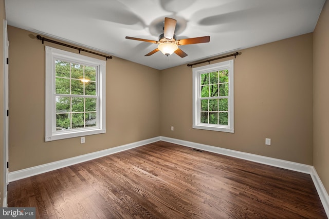 empty room featuring dark wood-style flooring, a ceiling fan, healthy amount of natural light, and baseboards