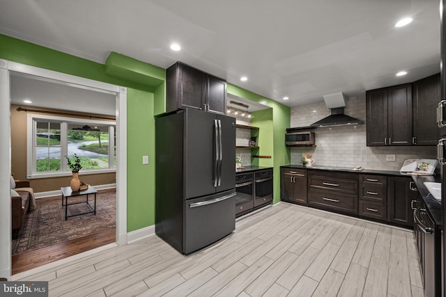 kitchen featuring appliances with stainless steel finishes, light wood-style flooring, wall chimney range hood, dark countertops, and decorative backsplash
