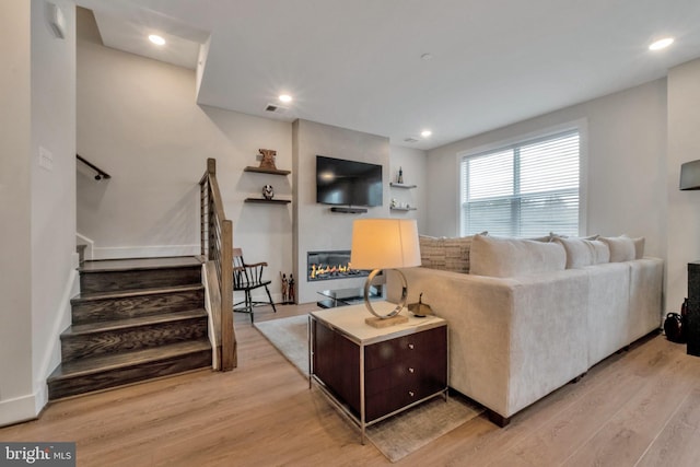 living room with a large fireplace, recessed lighting, light wood-style floors, and stairs
