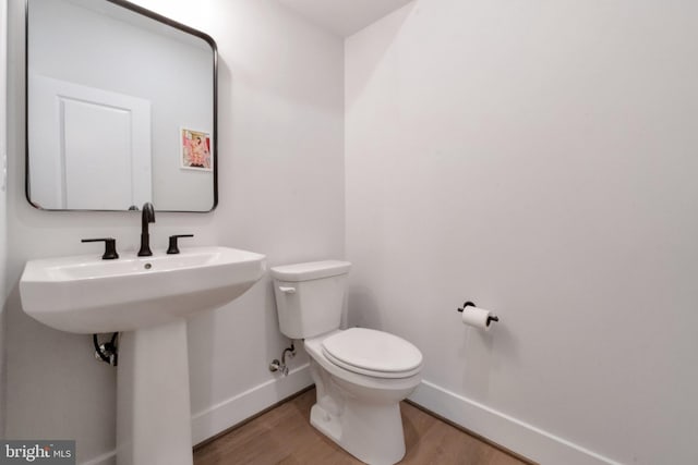 bathroom with toilet, baseboards, wood finished floors, and a sink