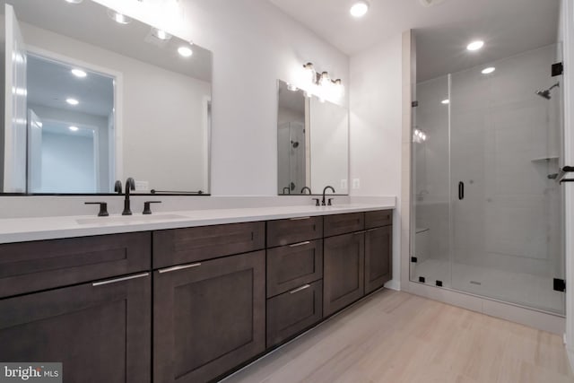 bathroom featuring double vanity, a sink, a stall shower, and wood finished floors