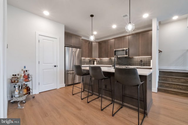kitchen featuring light wood-style flooring, light countertops, decorative backsplash, and appliances with stainless steel finishes