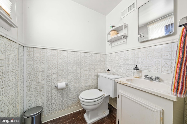 half bathroom with a wainscoted wall, vanity, toilet, and visible vents