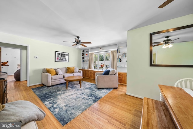 living area with baseboards, built in features, ceiling fan, and hardwood / wood-style floors
