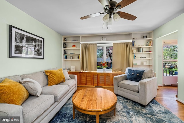 living room featuring a ceiling fan, built in features, and wood finished floors