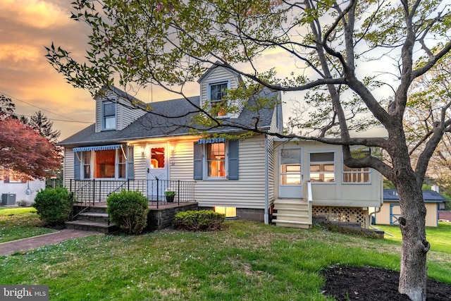 cape cod house featuring a shingled roof, a yard, and cooling unit