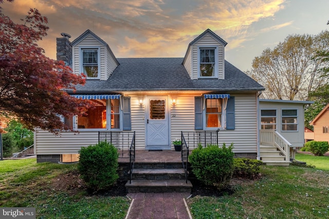 new england style home featuring a lawn, a porch, and roof with shingles