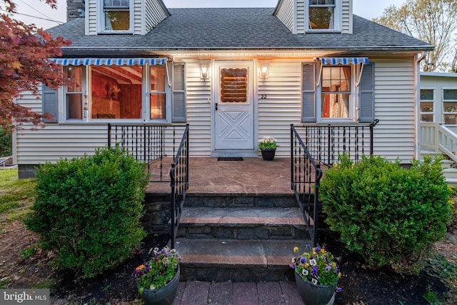 entrance to property with a shingled roof and a porch
