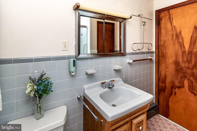 bathroom with tile walls, a wainscoted wall, vanity, and toilet