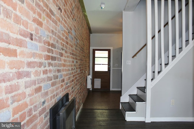 foyer with brick wall, wood finished floors, stairway, and baseboards
