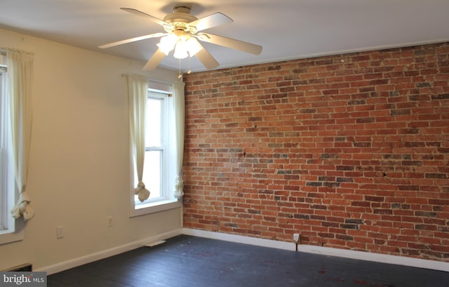 spare room with baseboards, dark wood-style floors, brick wall, and ceiling fan