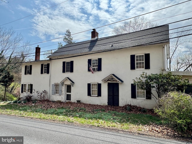 colonial home with a chimney, a shingled roof, and stucco siding