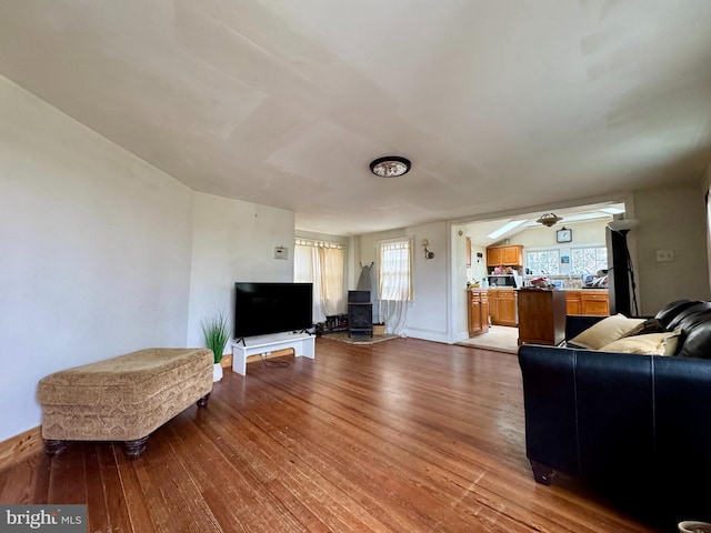 living room with a wood stove, a ceiling fan, and wood finished floors