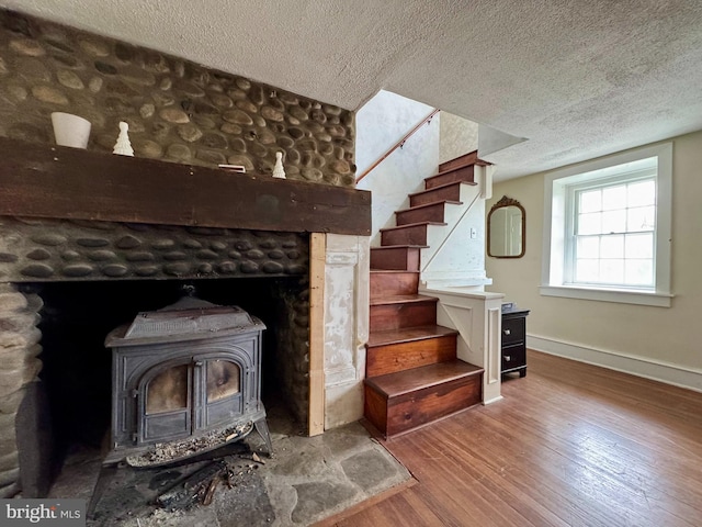 room details with a wood stove, a textured ceiling, baseboards, and wood finished floors