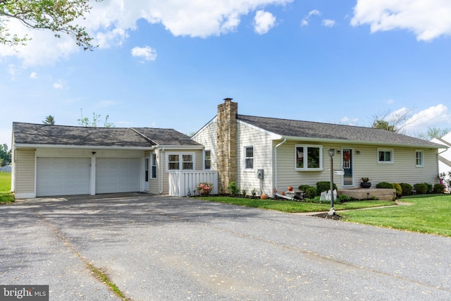 view of front of home with a garage, driveway, a chimney, and a front lawn