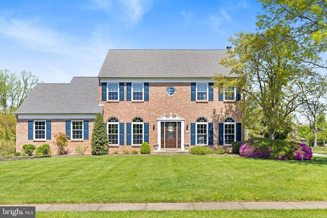 colonial inspired home with brick siding, a front lawn, and roof with shingles