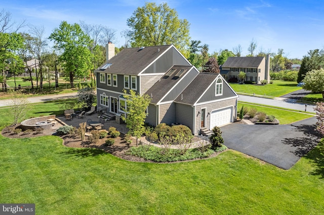 view of front of property with a shingled roof, a chimney, a front lawn, and aphalt driveway