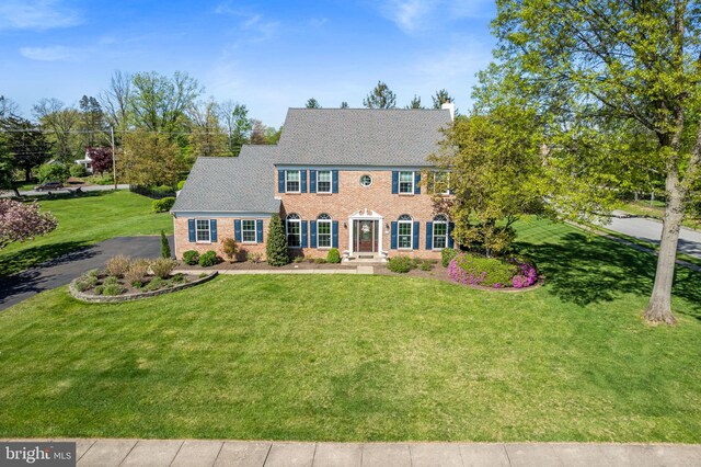 colonial inspired home featuring brick siding, a chimney, and a front yard