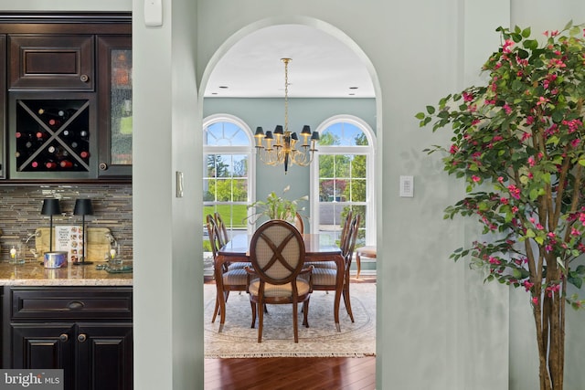 dining room featuring arched walkways, a notable chandelier, dark wood finished floors, and a dry bar