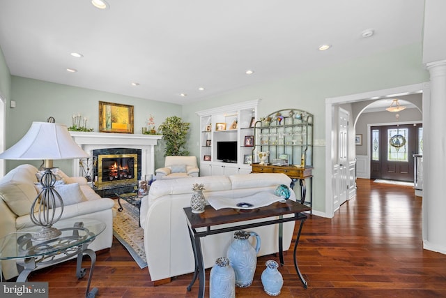 living room featuring recessed lighting, arched walkways, dark wood-style floors, and a premium fireplace