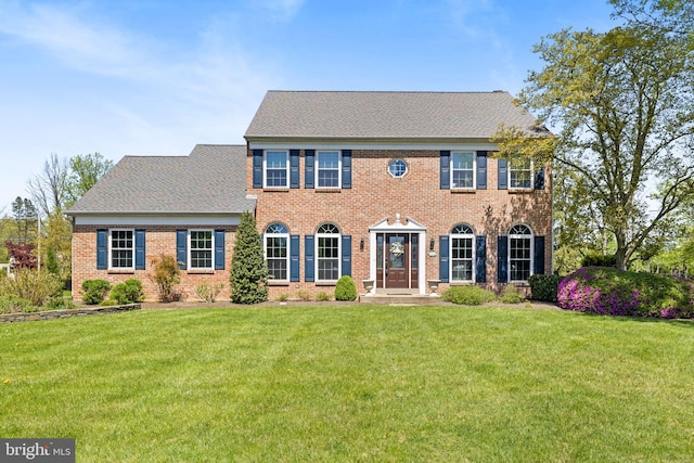 colonial-style house with brick siding, roof with shingles, and a front lawn