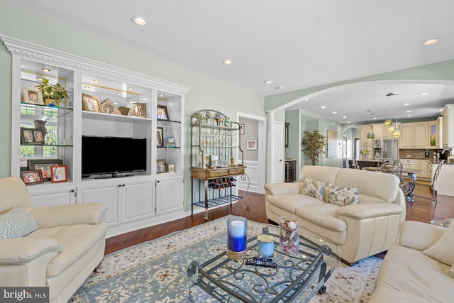 living area featuring built in features, wood finished floors, recessed lighting, ornate columns, and arched walkways