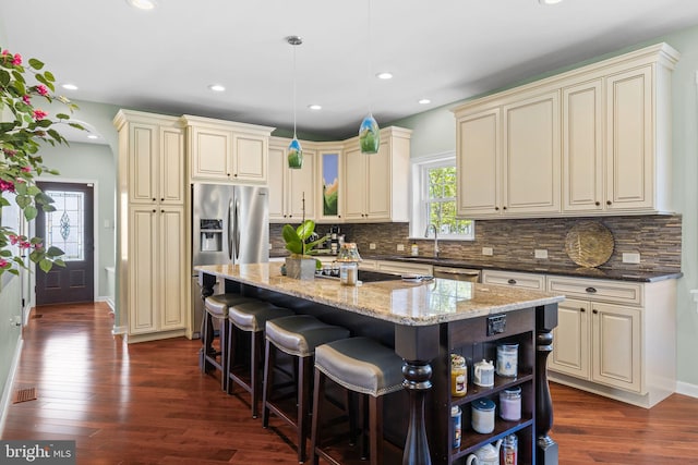 kitchen featuring cream cabinets, stainless steel appliances, light stone counters, and a center island
