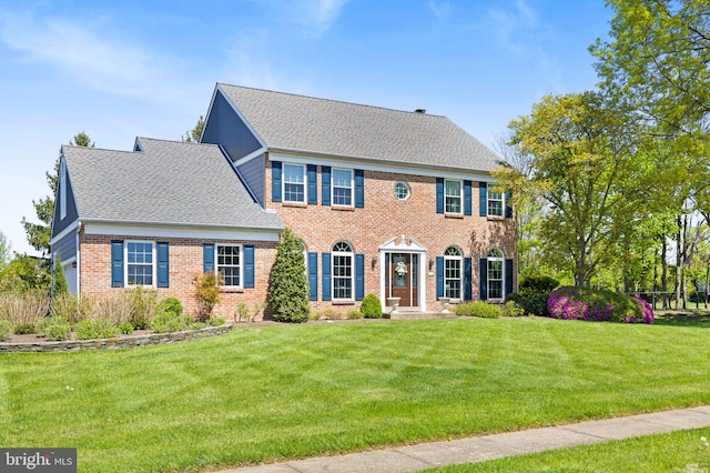 colonial home with brick siding, a shingled roof, and a front lawn