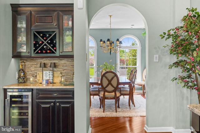 bar featuring tasteful backsplash, dark wood finished floors, a bar, a notable chandelier, and wine cooler