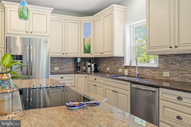 kitchen featuring backsplash, cream cabinets, a sink, dark stone countertops, and stainless steel appliances