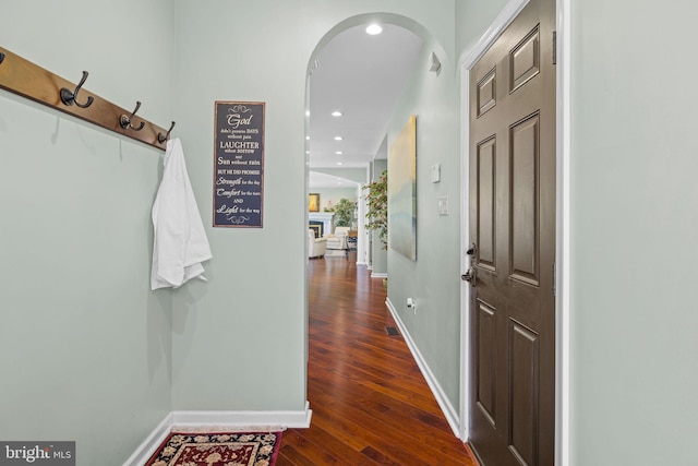 corridor featuring baseboards, arched walkways, dark wood-type flooring, and recessed lighting
