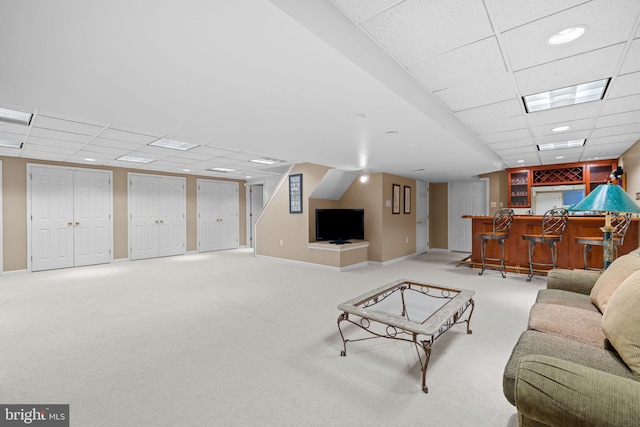 living room featuring carpet floors, baseboards, indoor wet bar, and a paneled ceiling