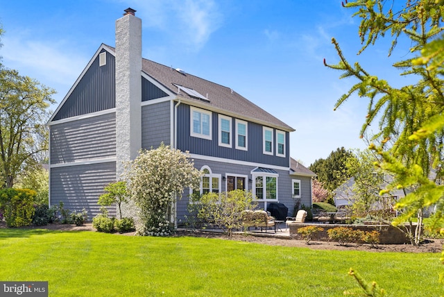 back of house featuring a lawn, a patio, a chimney, and roof with shingles