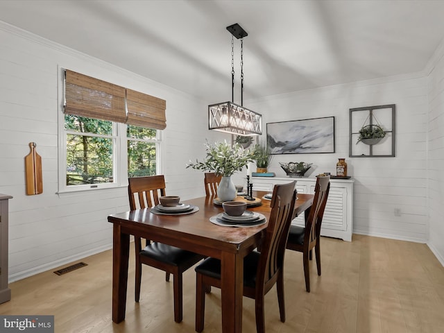 dining area with light wood finished floors, ornamental molding, a chandelier, baseboards, and wood walls