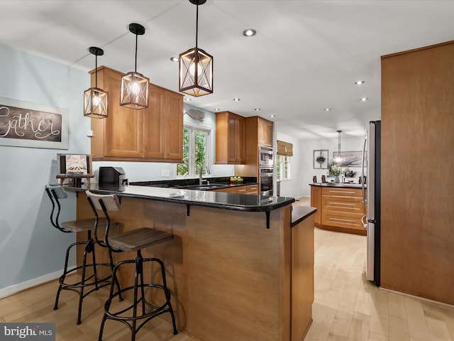 kitchen featuring a peninsula, brown cabinets, a sink, appliances with stainless steel finishes, and light wood-type flooring