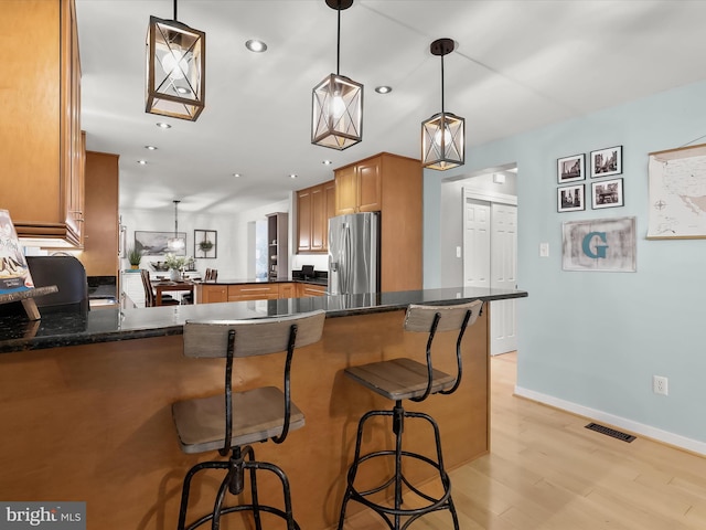 kitchen featuring stainless steel fridge, a peninsula, brown cabinets, light wood finished floors, and a kitchen bar