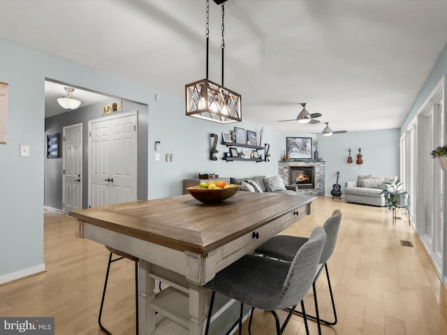 dining area with ceiling fan, light wood-style flooring, a stone fireplace, and baseboards